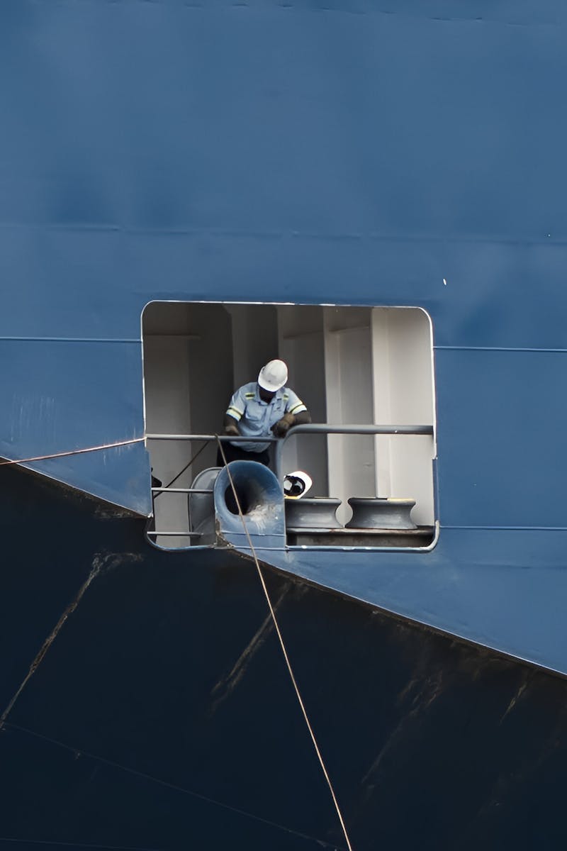 A worker performs maintenance on a large ship's side, highlighting marine industry operations.